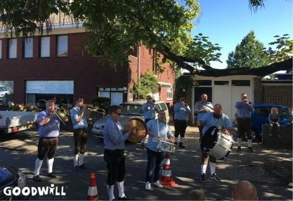 A marching band performing outdoors, dressed in traditional blue and white outfits, playing brass and percussion instruments.