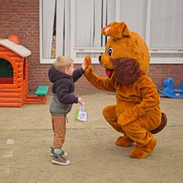 A young child giving a high-five to a person in a brown dog mascot costume outdoors.