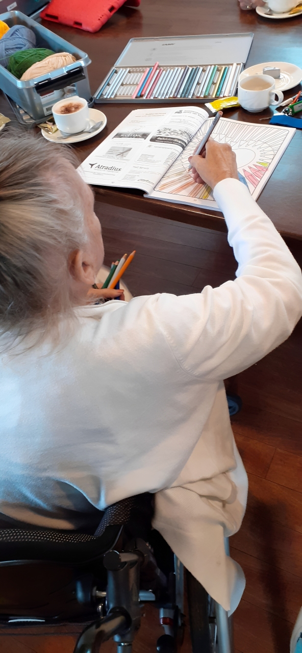An elderly person in a wheelchair coloring with colored pencils at a table.