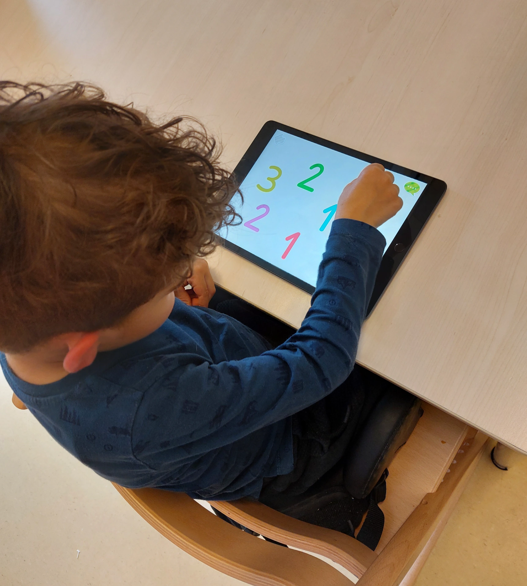 A young boy sitting at a table using a tablet with colorful numbers displayed on the screen.